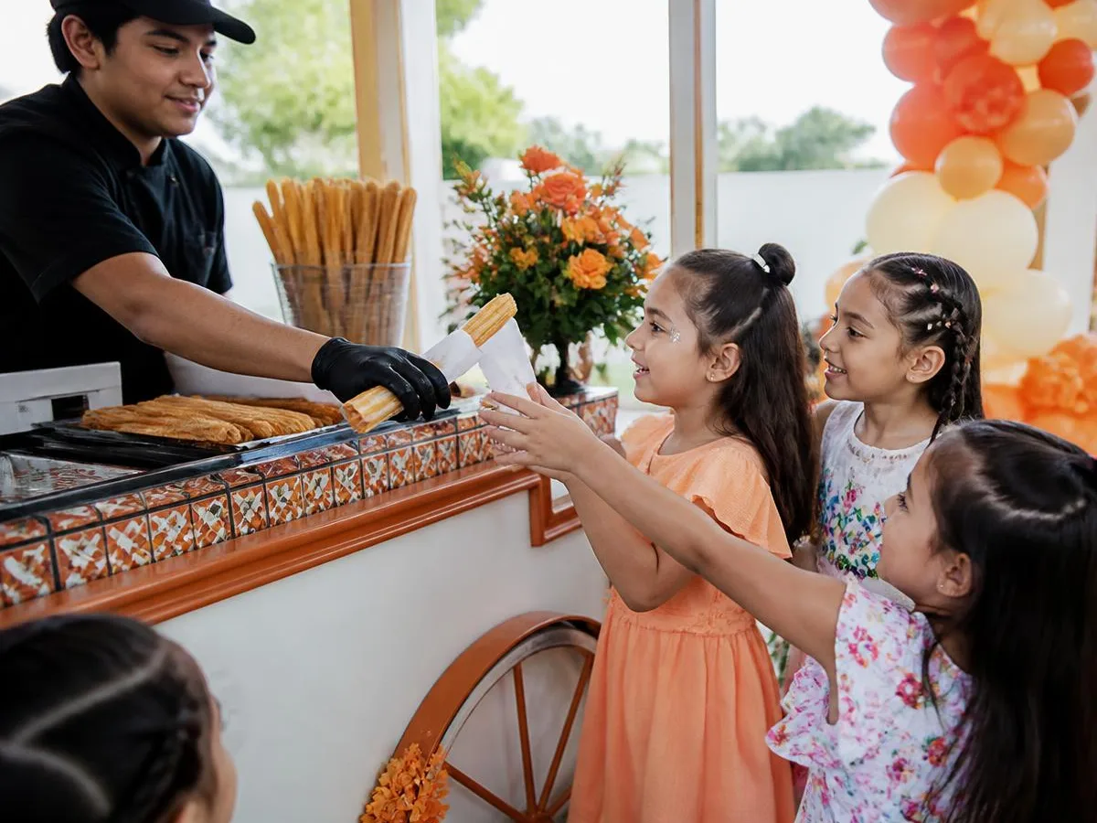 Crianças recebendo churros quentinhos em um carrinho colorido durante festa infantil