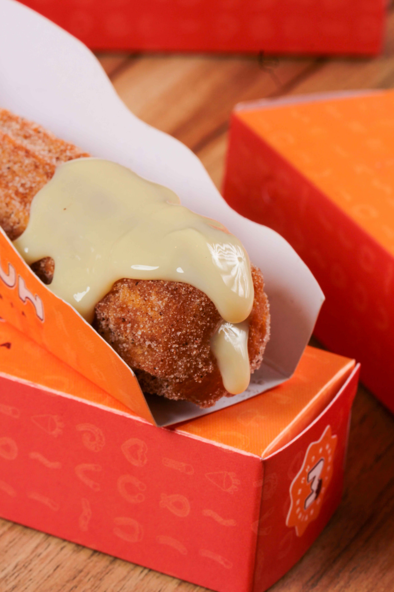 Churros Maneluh com cobertura cremosa na embalagem laranja da churreria